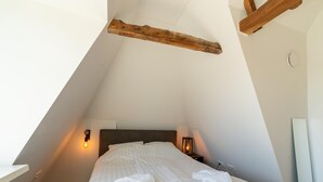 A bedroom with a sloped ceiling, a wooden beam, a bed with white linens, two bedside lamps, and a bedside table. - Modern Renovated Apartment in the Heart of Sneek (Sneek)