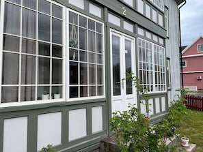A two-story building with a green and white exterior, numbered 2, featuring large windows and a small garden area with potted plants. - 4 Person Holiday Home in Sodra vi (Sodra Vi)