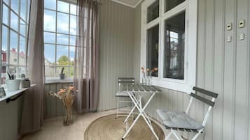 A room with a large window, a table, two chairs, and a woven rug.