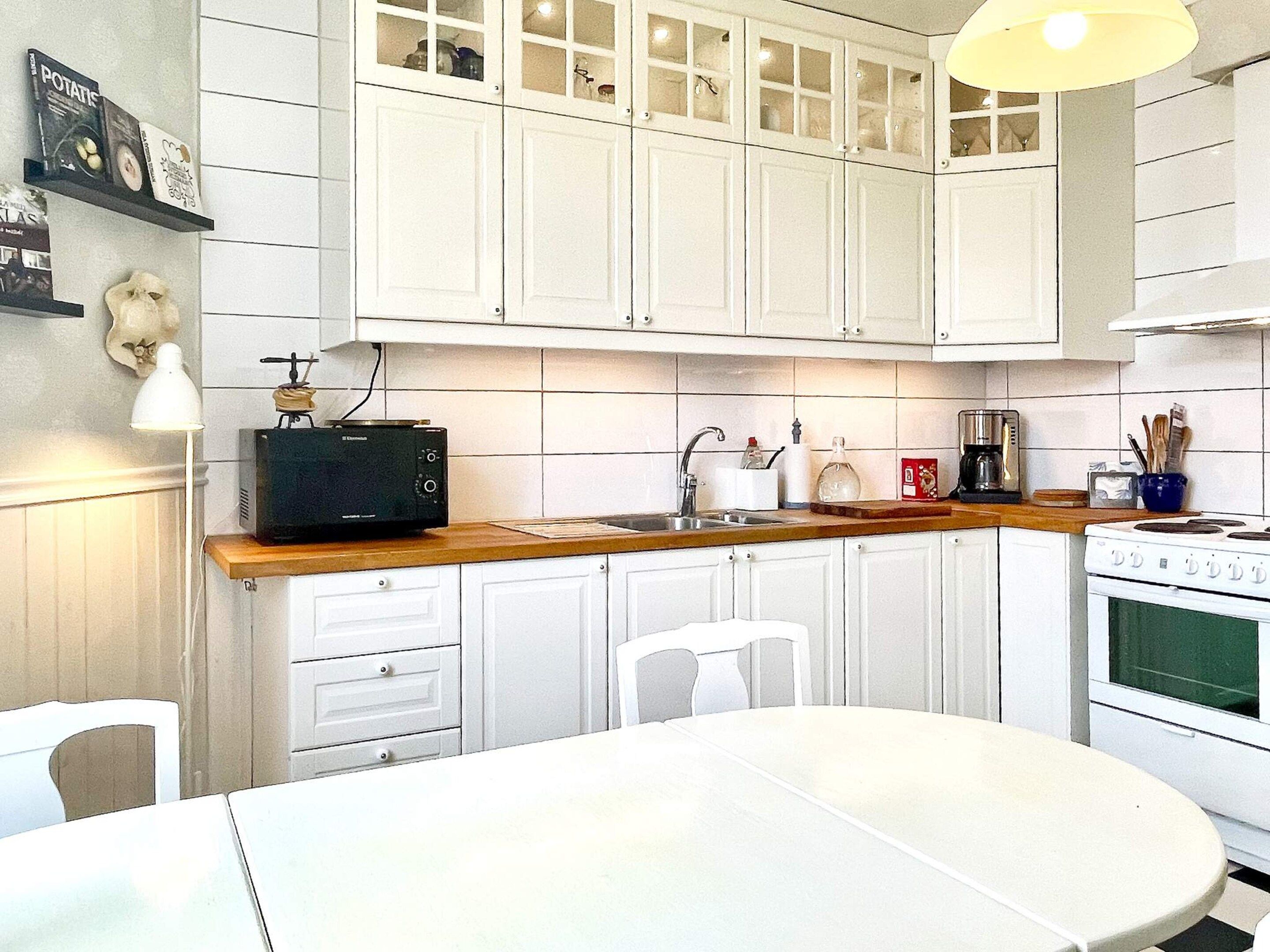 Una cocina con armarios blancos, microondas, estufa y una mesa de comedor.