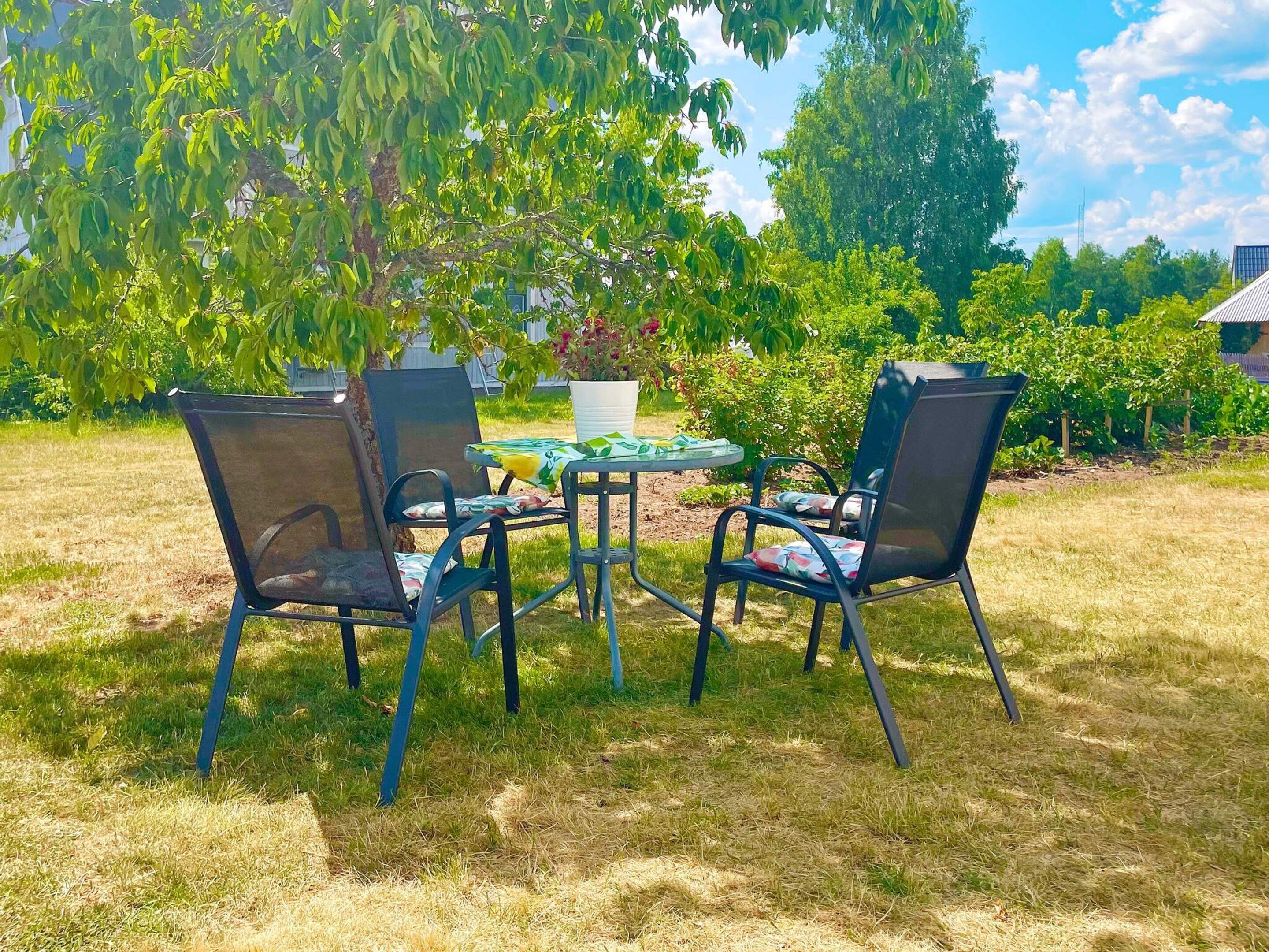 An outdoor seating area with a round table and four chairs, surrounded by grass and trees.