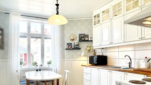 A kitchen with white cabinets, a black and white checkered floor, a round dining table with chairs, and a hanging light fixture. - 4 Person Holiday Home in Sodra vi (Sodra Vi)