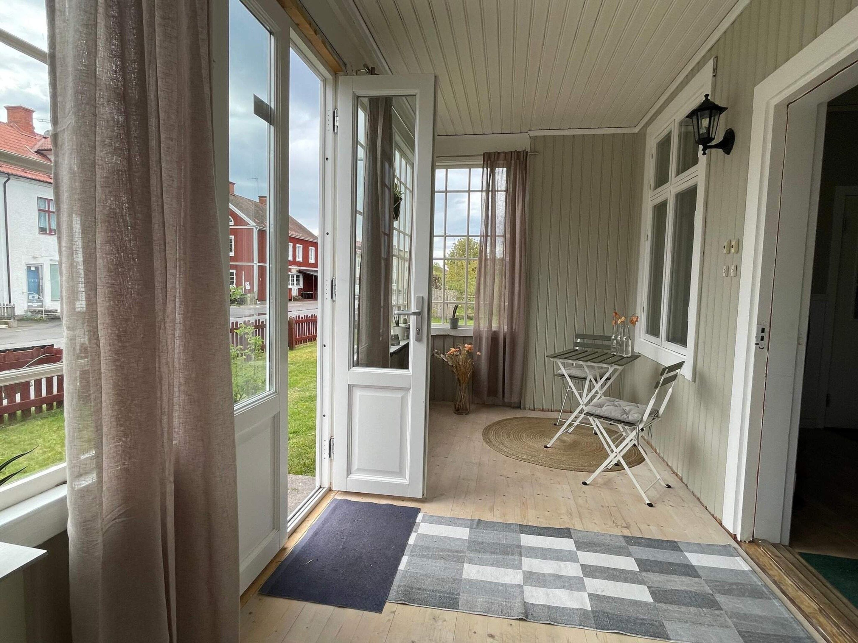A room with a wooden floor, a checkered mat, a folding chair, and a table with a vase of flowers.