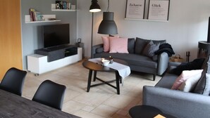 Un salon moderne avec un canapé gris, une table basse, un téléviseur et une bibliothèque.