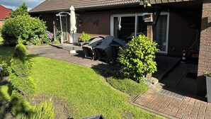 A residential house with a tiled roof, a covered patio area with outdoor furniture, and a well-maintained garden. - Ferienhaus mit Blick in die Weite Wiesenlandschaft 5 Min.vom Natursee Entfernt (Hage)