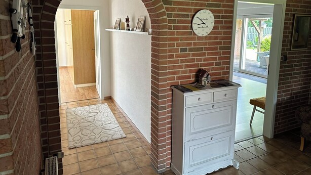 A hallway with a brick wall, a white dresser, a clock, and a door leading outside. - Ferienhaus mit Blick in die Weite Wiesenlandschaft 5 Min.vom Natursee Entfernt (Hage)