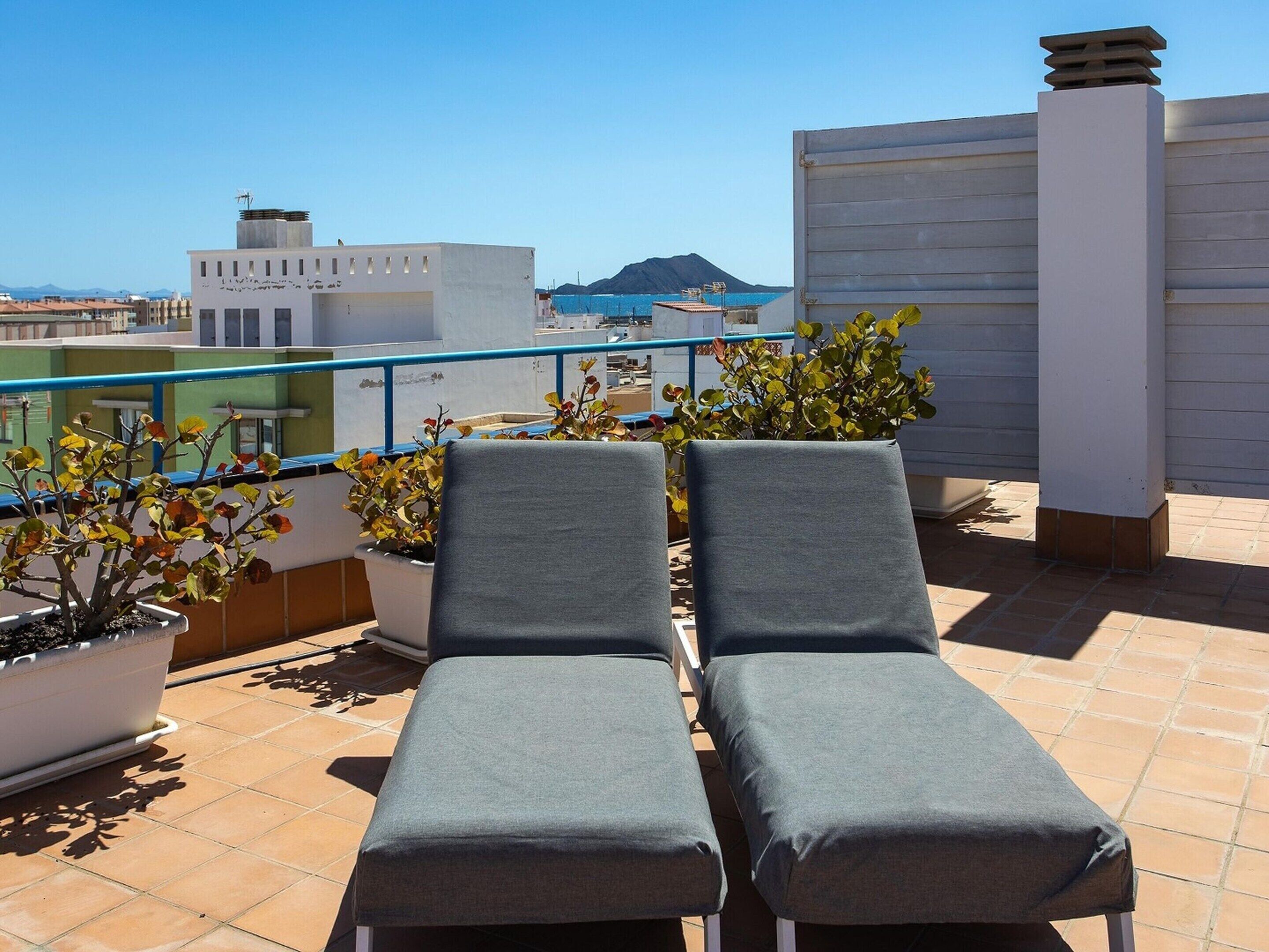 Une terrasse sur le toit, dotée de deux chaises longues, de plantes en pot et offrant une vue sur la mer et les montagnes lointaines.