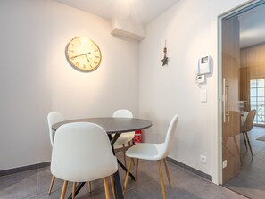 A dining area with a round table and four white chairs, a wall-mounted clock, and a small decorative item. - Family Holiday Home, Westende (Middelkerke)