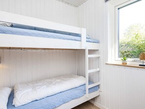 Un lit superposé avec une literie blanche et bleue, une fenêtre donnant sur un paysage verdoyant et une petite plante posée sur le rebord de la fenêtre.