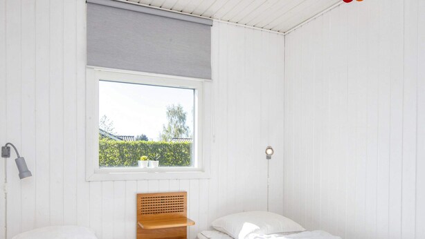 A small, white room with two beds, a window with a view of greenery, and a wooden shelf. - 5 Person Holiday Home in Sydals (Sydals)