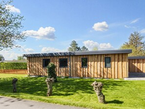 Un bâtiment moderne en bois, doté d’un toit plat, de deux fenêtres et d’une pelouse bien entretenue, avec de l’herbe taillée et des arbres taillés en forme.