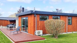 Ein modernes Holzhaus mit einer Terrasse, Gartenmöbeln und einem kleinen Baum.