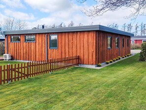 A modern wooden building with a flat roof, a fenced yard, and a clear sky. - 5 Person Holiday Home in Sydals (Sydals)