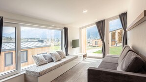 A spacious living room with large windows, a built-in bench, a sofa, and a flat-screen TV. - Modern Chalet With air Conditioning (Kotschach-Mauthen)