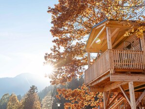 A wooden cabin with a balcony, surrounded by autumn foliage and mountains in the background. - Modern Chalet With air Conditioning (Kotschach-Mauthen)