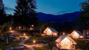 A series of cabins with a stone pathway leading to them, surrounded by trees and a mountainous backdrop. - Modern Chalet With air Conditioning (Kotschach-Mauthen)