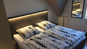 A bed with a geometric patterned bedspread and matching pillows, a wooden headboard, and a mirror on the wall. - Seepark Burhave Haus 8 (Butjadingen)