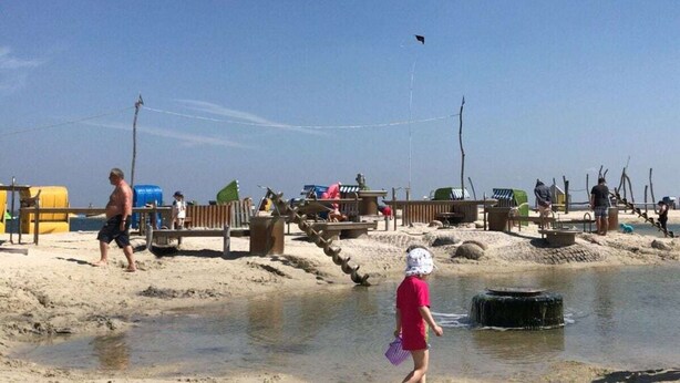 A sandy beach with a small water feature and wooden structures. - Seepark Burhave Haus 8 (Butjadingen)