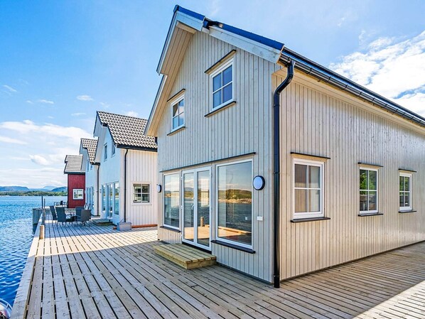A modern house with a wooden deck and large windows, overlooking a body of water.