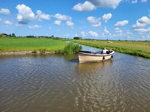 Un bateau sur une rivière paisible, avec un paysage verdoyant et quelques nuages épars dans le ciel.