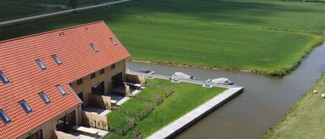 A riverside building with a red roof, a patio area, and a view of the river.