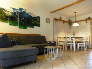 A living room with a grey sofa, a dining table with white chairs, and two round wire tables with wine glasses. - Sandra Comfortable Holiday Residence (Lechbruck)