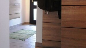 A hallway with a wooden wardrobe, a coat rack with a jacket, and a small rug on the floor. - Sandra Comfortable Holiday Residence (Lechbruck)