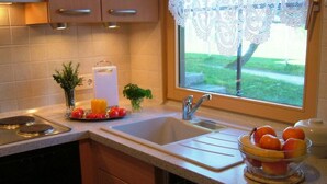 A kitchen with a sink, a window with lace curtains, and a bowl of fruit on the counter. - Sandra Comfortable Holiday Residence (Lechbruck)