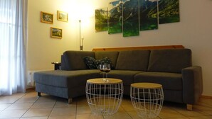 A living room with a grey sofa, two wireframe coffee tables, and a large window with curtains. - Sandra Comfortable Holiday Residence (Lechbruck)