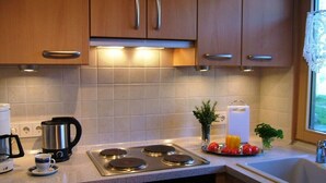 A kitchen with wooden cabinets, a stove, a coffee maker, and a sink. - Sandra Comfortable Holiday Residence (Lechbruck)