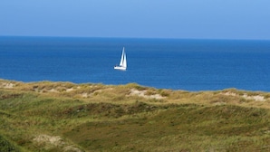 A sailboat on the ocean with a grassy beach in the foreground. - 6 in het Huis Meerloft (Norderney)