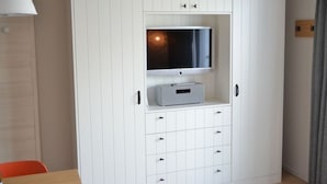 A room with a white wardrobe, a television on a shelf, and a small table with a chair. - 6 in het Huis Meerloft (Norderney)