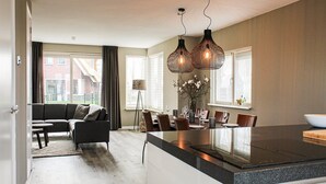 A modern kitchen with a central island, dining area with chairs, and a sofa in a living area with a view of the outside. - Villa With Garden, in a Holiday Park (Idskenhuizen)