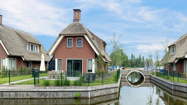 A canal-side residential area with brick houses, a small bridge, and a calm water body reflecting the buildings. - Villa With Garden, in a Holiday Park (Idskenhuizen)