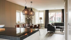 A modern kitchen with a central island, dining area with chairs and a table, and a living room with a sofa and coffee table. - Villa With Garden, in a Holiday Park (Idskenhuizen)