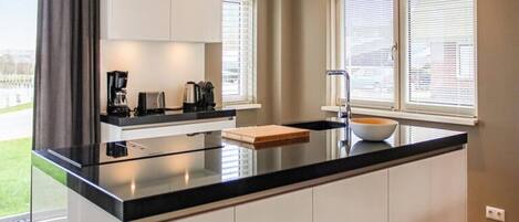 A modern kitchen with a black countertop, white cabinets, and a large window with blinds.
