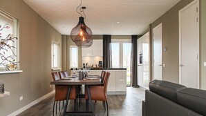 A modern kitchen with white cabinets, a dining table with chairs, and a hanging light fixture. - Villa With Garden, in a Holiday Park (Idskenhuizen)