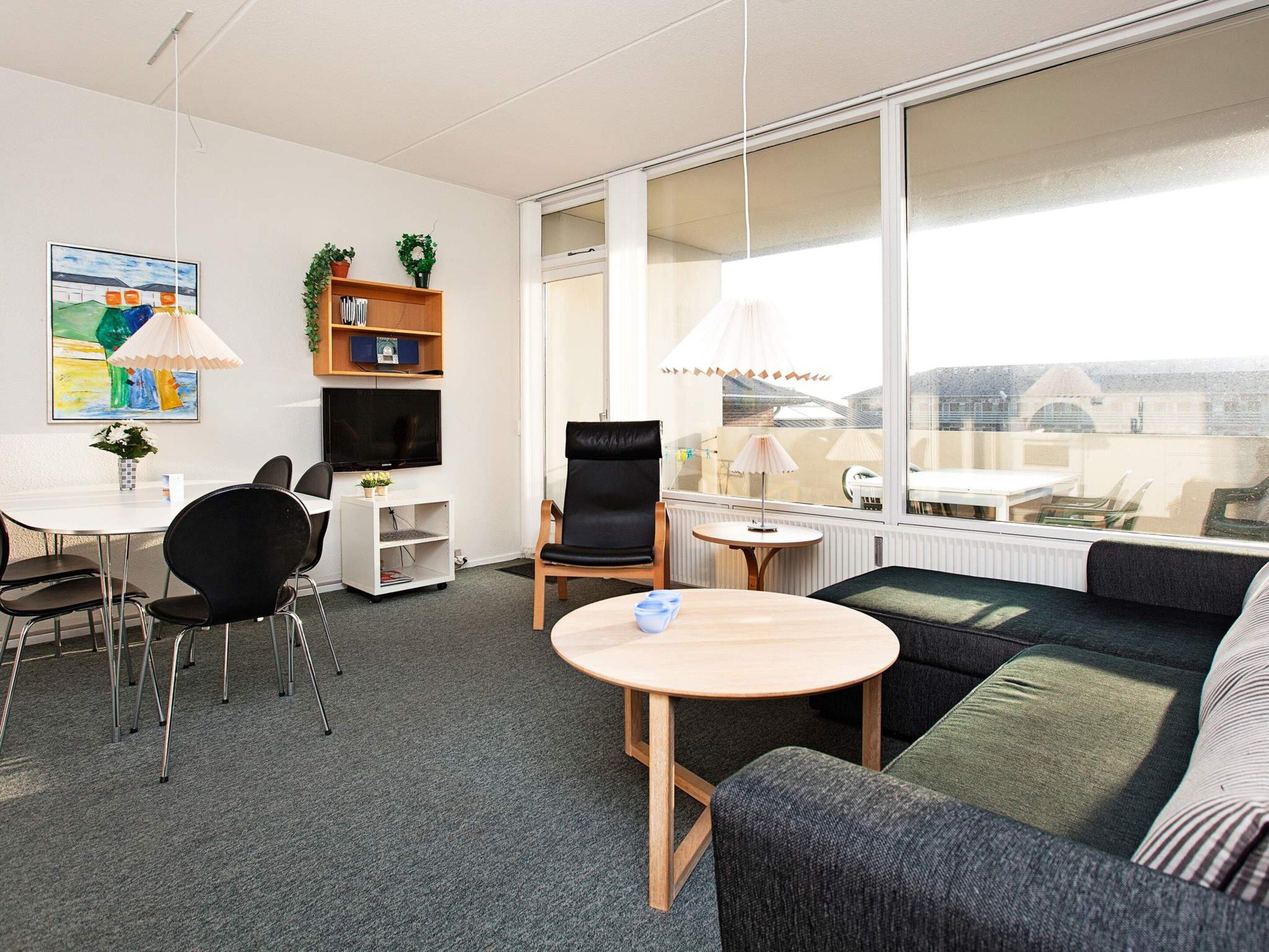 A modern living room with a sofa, chairs, a small table, a TV, and a bookshelf.