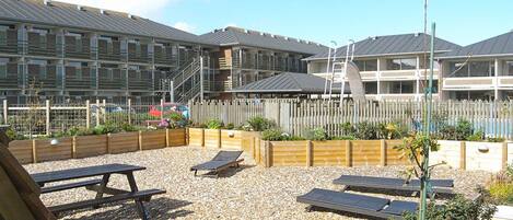 A courtyard with outdoor seating, a wooden fence, and a building with multiple windows and balconies in the background.