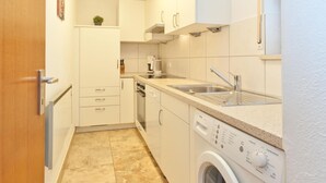 A compact kitchen with white cabinets, a built-in oven, a dishwasher, and a washing machine. - Family Escape With Pool (Nesselwang)