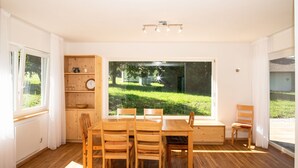 A dining area with a large window, wooden furniture, and a built-in bookshelf. - Family Escape With Pool (Nesselwang)