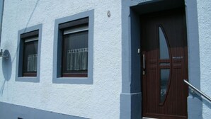 A building with a blue exterior, a dark brown door, and two windows with curtains. - Muller Comfortable Holiday Residence (Lutzkampen)