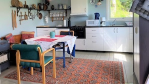 Cocina compacta con armarios blancos, microondas y cafetera. Hay una zona de comedor con mesa y sillas, y una alfombra estampada en el suelo.