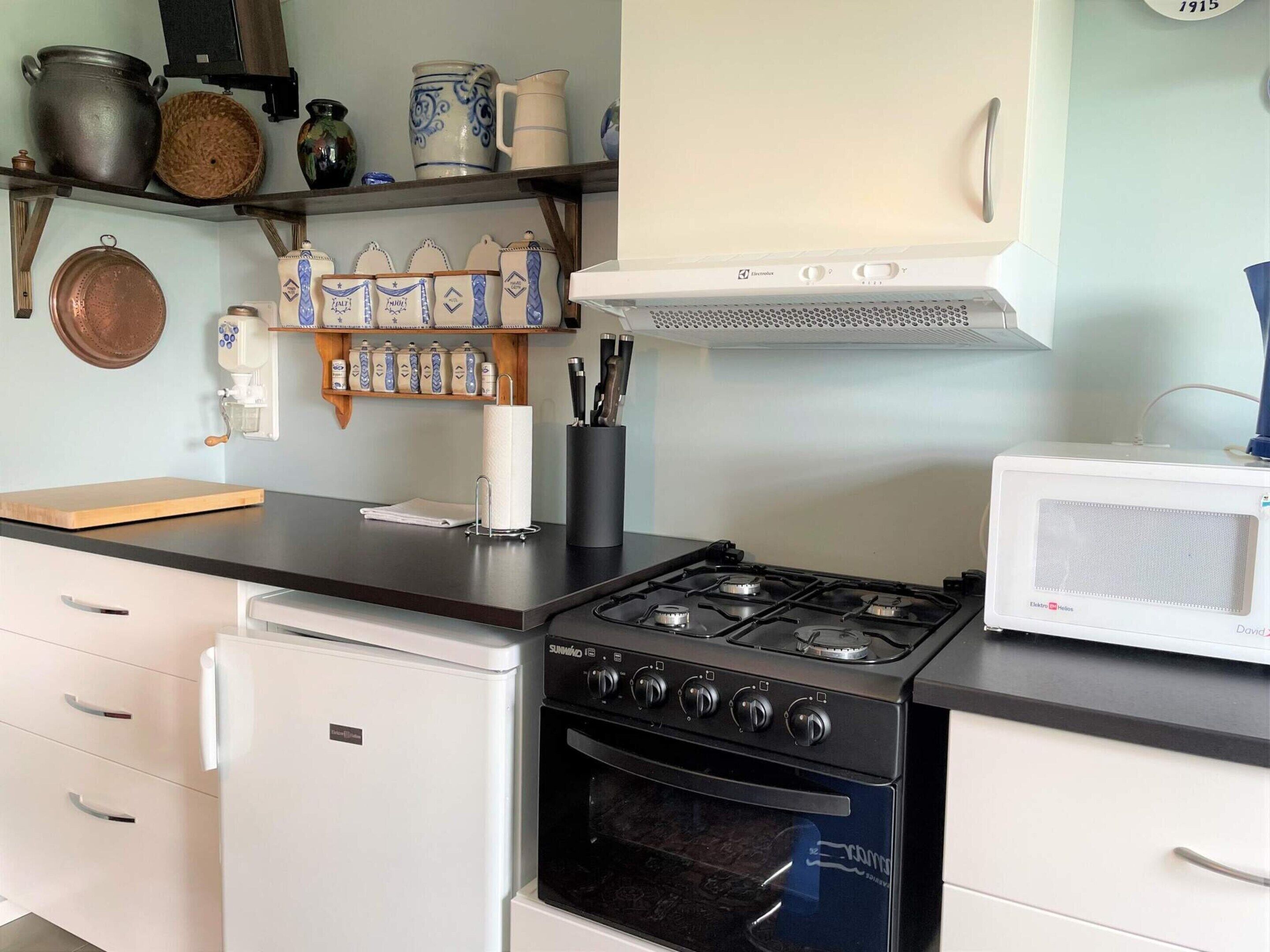 A kitchen with a stove, oven, microwave, and various kitchen utensils on shelves.