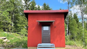 Una cabaña de madera roja con una puerta oscura, un pequeño porche y un camino de grava que conduce a la entrada.