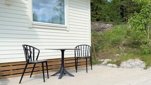 Un patio al aire libre con dos sillas de metal negro y una mesa pequeña, frente a un edificio blanco con una ventana.