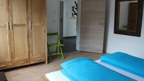 A bedroom with a wooden wardrobe, a green chair, a bed with blue bedding, and a mirror on the wall. - Holiday Home "max & Moritz" (Bammental)