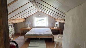 Un pequeño dormitorio en el ático con techo inclinado, una cama individual, dos mesitas de noche con lámparas, un ventanal con cortinas y suelo de madera.