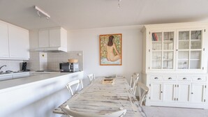 A kitchen with white cabinets, a dining table with chairs, and a large cabinet with glass doors. - Apartment on Beach Near Town Center (Koksijde)