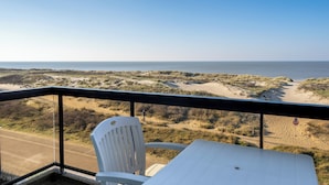 A balcony with a white chair and table overlooking a beach and dunes. - Apartment on Beach Near Town Center (Koksijde)